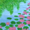 pink lotus flowers float on a light blue pond with dark green lily pads, there is a lighter green tree with leaves overhanging the water